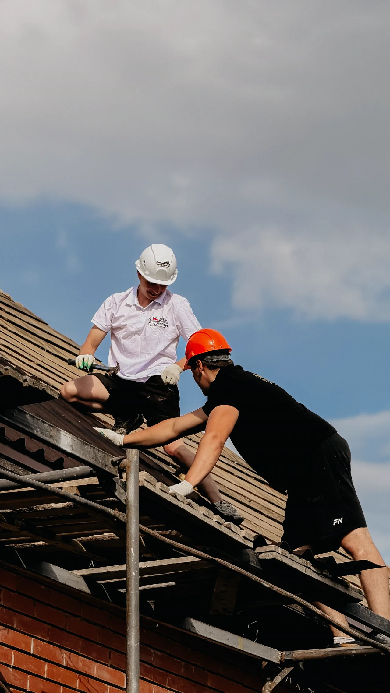 Two roofers at work on a house roof under a blue sky