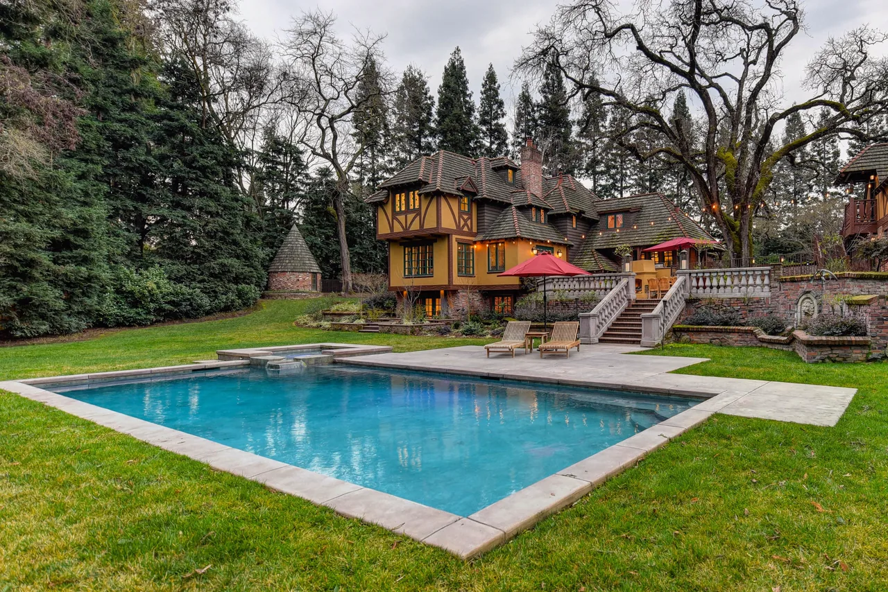 A backyard pool on a green lawn in front of a large house