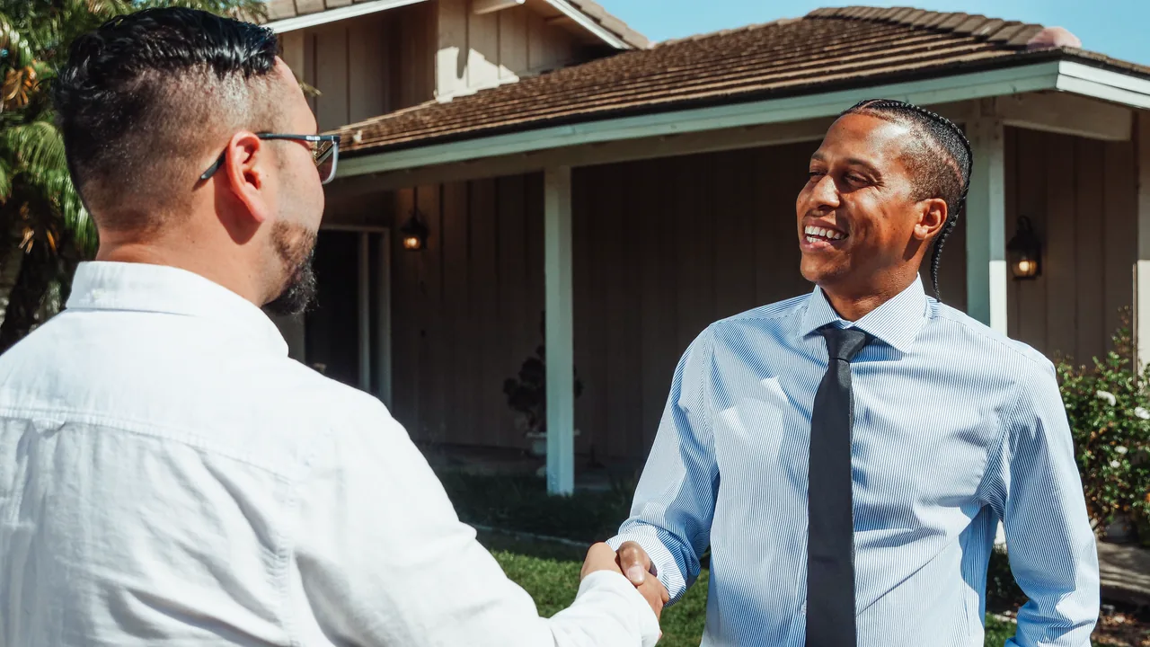 A real estate agent shaking hands with a buyer in front of a house